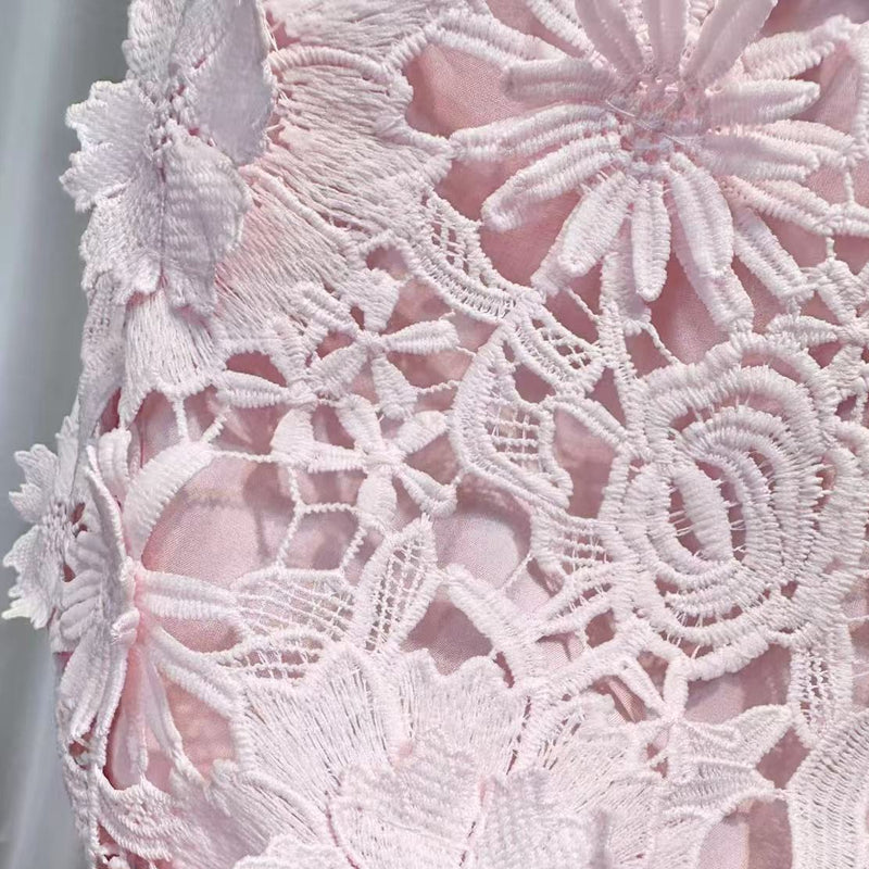 Close-up of white lace fabric held by a hand against a neutral background